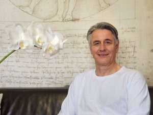 Heilpraktiker Kuhnhenne sitzt im Behandlungsraum auf der Couch und lächelt.